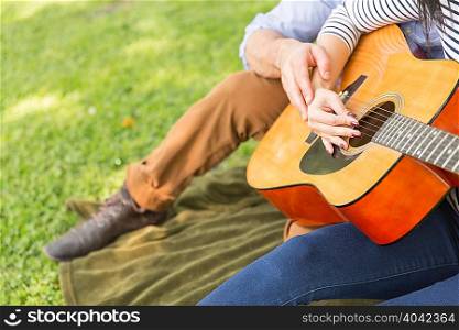 Cropped view of couple sitting on grass playing acoustic guitar