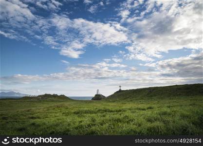 Cross in landscape of Ynys Llanddwyn Island with Twr Mawr lighthouse in background