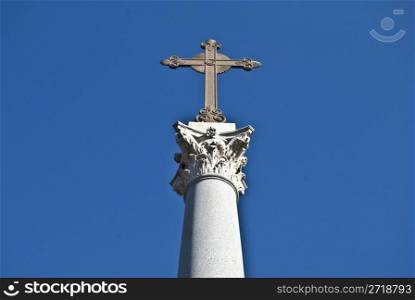 cross on a corinthian pillar against a blue sky