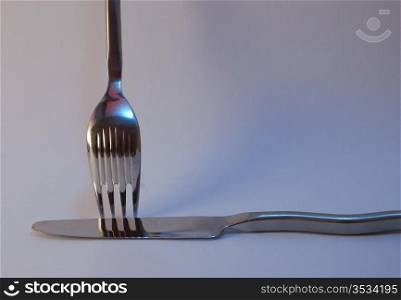 Crossed knife and fork with reflections on soft blue background