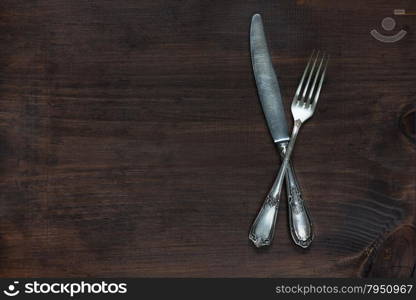 Crossed vintage fork and knife on old wooden board