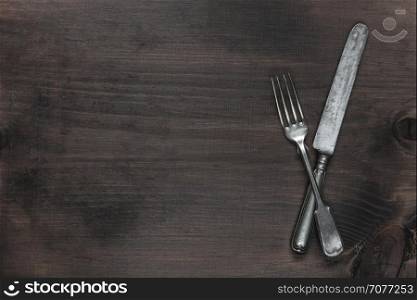Crossed vintage silver fork and knife on the background of old brown wooden board, with copy-space