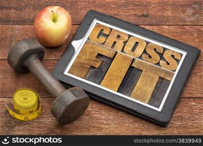 crossfit word abstract - text in letterpress wood type on a digital tablet with dumbbell and tape measure - fitness concept