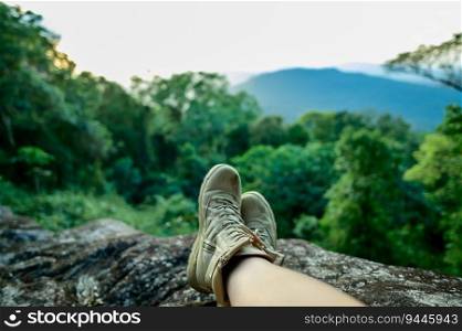 Crossing legs of traveler sitting relax on high mountain top in forest, beautiful landscape on valley, cloud and woodland, copy space, trekking and hiking concept