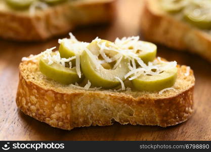 Crostini with green olive slices and freshly grated parmesan-like hard cheese, photographed with natural light (Selective Focus, Focus on the front of the first olive slices)