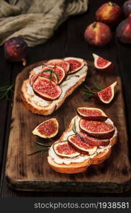 Croutons with figs and cream cheese on a wooden board, closeup view, selective focus. Snack idea. Close-up on healthy food