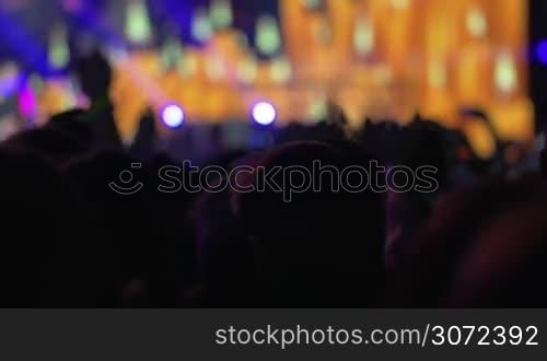 Crowd of fans on the concert. Favorite music rhythms making feel the energy and dance. Illuminated colorful stage in background