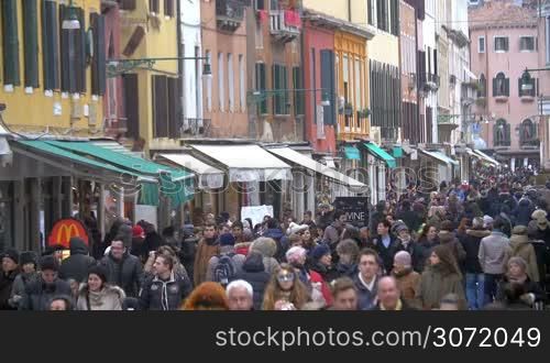 Crowd of people in the street of old Italian city. People passing by vintage buildings with stores and cafes
