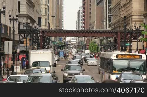 Crowded Chicago city center of vehicles and pedestrians. Loop life on a weekday with the elevated underground trains crossing. Lots of cars and commuters in Illinois. Human activity on the streets of Chicago.
