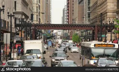 Crowded Chicago city center of vehicles and pedestrians. Loop life on a weekday with the elevated underground trains crossing. Lots of cars and commuters in Illinois. Human activity on the streets of Chicago.