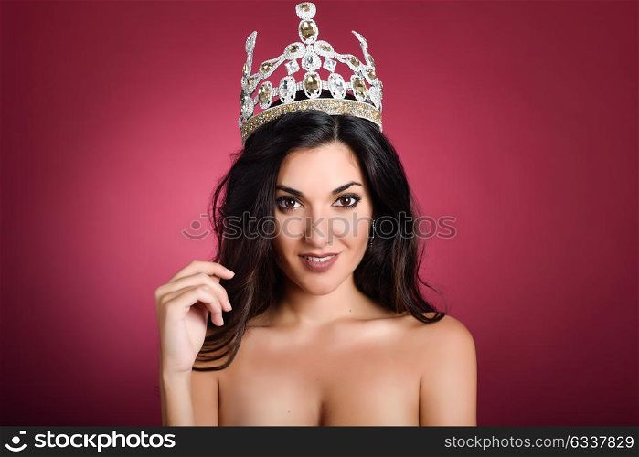 Crowned woman like miss of beauty looking at camera isolated on red wine background. Girl wearing crown, studio shot.