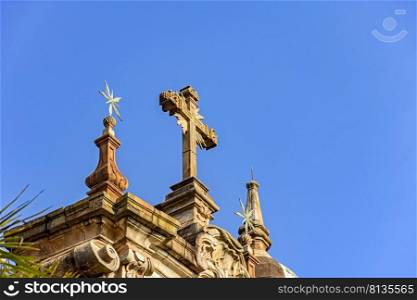 Crucifix and ornaments on top of the facade of an old and historic baroque church in the city of Ouro Preto in Minas Gerais. Crucifix and ornaments on top of the facade of an old and historic baroque church