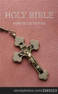 Crucifix lying on cover of closed Holy Bible.