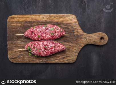 Crude kebab on a skewer on vintage cutting board on wooden rustic background top view close up