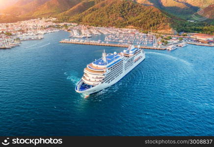 Cruise ship at harbor. Aerial view of beautiful large white ship at sunset. Colorful landscape with boats in marina bay, sea, green forest. Top view from drone of yacht. Luxury cruise. Floating liner