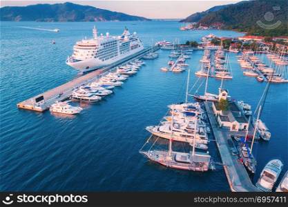 Cruise ship at harbor. Aerial view of beautiful large white ship at sunset. Colorful landscape with boats in marina bay, sea, colorful sky. Top view from drone of yacht. Luxury cruise. Floating liner. Aerial view of beautiful large white ship at sunset
