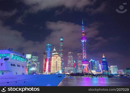 Cruise ship in harbor by Shanghai downtown, skyscrapers of modern architecture and tv tower illuminated at night, China