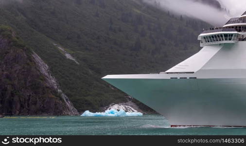 Cruise ship sailing in Alaska among icebergs. Ship's bow with mountains and cloud in the background.
