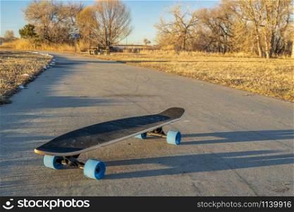 cruising longboard with blue wheels on a paved bike trail in winter scenery in northern Colorado - Boyd Lake State Park