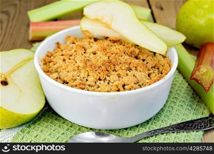 Crumble with pears and rhubarb in a white bowl on a napkin, stalks of rhubarb and pear, spoon on a wooden boards background