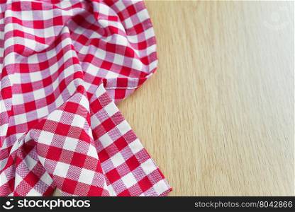 Crumpled cotton checked red and white tablecloth lies on the edge of wooden table