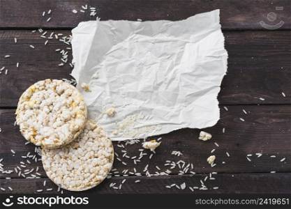 crumpled paper with two round puffed rice cake with grains wooden desk