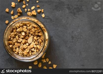 Crunchy almond and oatmeal granola in jar, photographed overhead on slate with natural light (Selective Focus, Focus on the top of the granola)