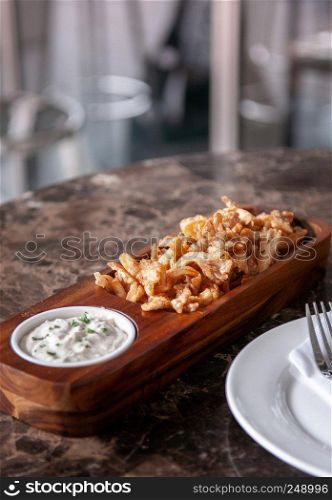 Crunchy deep fried calamari with Tartar sauce in hard wood plate on marble table, close up shot