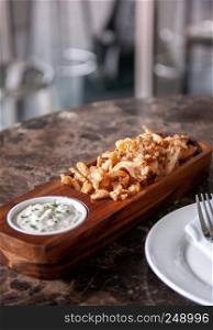 Crunchy deep fried calamari with Tartar sauce in hard wood plate on marble table, close up shot