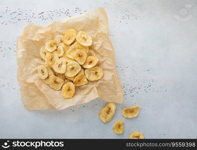 Crunchy dried banana chips on baking paper on light background.