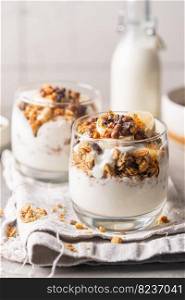 Crunchy granola with yogurt, banana, nuts, chocolate and honey in a glass on white background. Healthy breakfast concept.. Crunchy honey granola