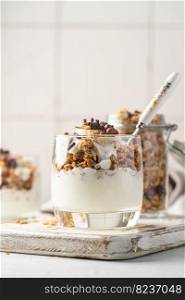 Crunchy granola with yogurt, banana, nuts, chocolate and honey in a glass on white background. Healthy breakfast concept.. Crunchy honey granola