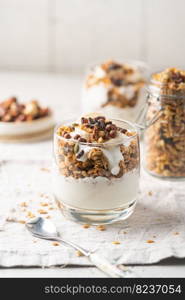 Crunchy granola with yogurt, banana, nuts, chocolate and honey in a glass on white background. Healthy breakfast concept.. Crunchy honey granola