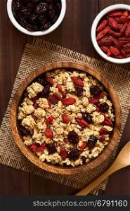Crunchy oatmeal cereal with almond and dried goji berries and cranberries in wooden bowl, photographed overhead on dark wood with natural light (Selective Focus, Focus on the top of the cereal and the berries)