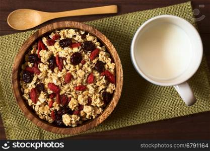 Crunchy oatmeal cereal with almond and dried goji berries and cranberries in wooden bowl with a cup of milk on the side, photographed overhead with natural light (Selective Focus, Focus on the top of the cereal)