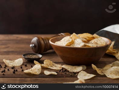 Crunchy potato crisps chips snack with black pepper in wooden bowl on dark table background with mill and ground pepper.