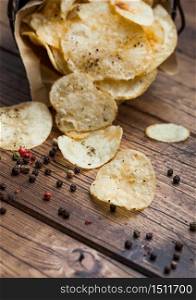 Crunchy potato crisps chips with black pepper in steel snack bucket on wooden table background. Macro