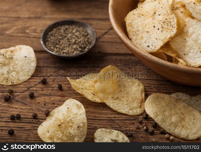 Crunchy potato crisps chips with black pepper in wooden bowl on wooden background. Macro