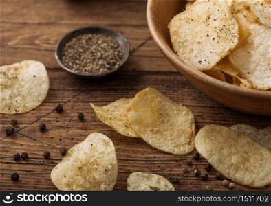Crunchy potato crisps chips with black pepper in wooden bowl on wooden background. Macro