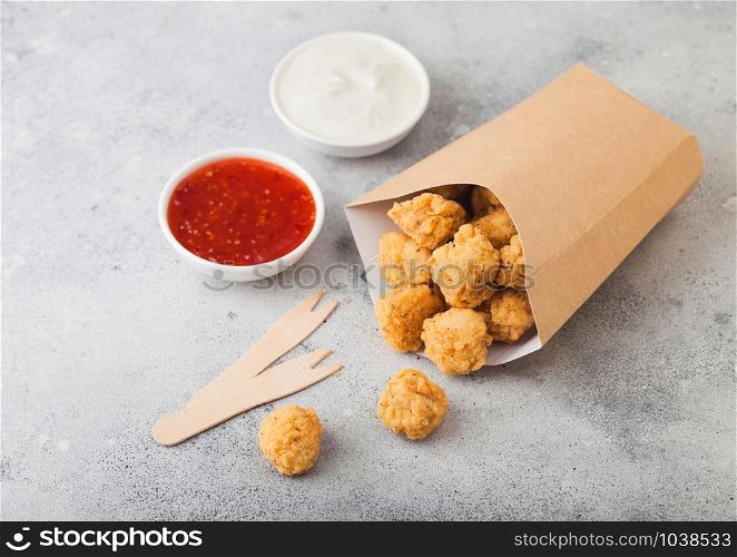 Crunchy southern chicken popcorn bites in paper container for fast food meals on light background.