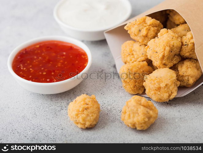 Crunchy southern chicken popcorn bites in paper container for fast food meals on light background. Macro