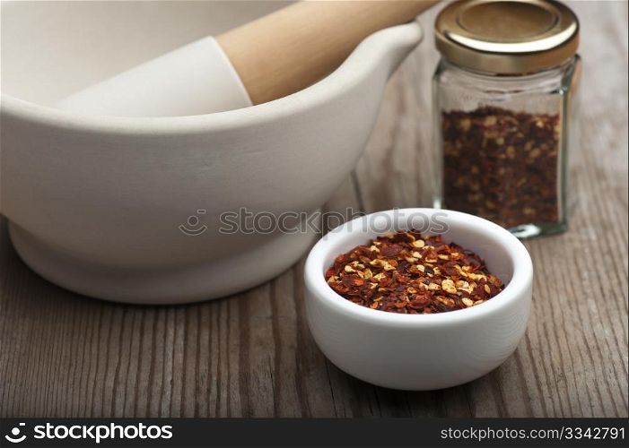 Crushed Chillies In A White Dish, With A Mortar and Pestle and Spice Jar, On A Wooden Kitchen Table