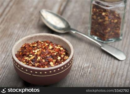 Crushed Chillies In An Old Dish, With Spice Jar And Spoon, On A Wooden Kitchen Table