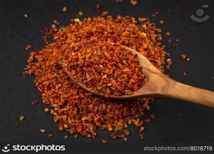 Crushed red chili pepper and wooden spoon on dark stone
