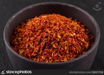 Crushed red chili pepper in stone bowl on dark background