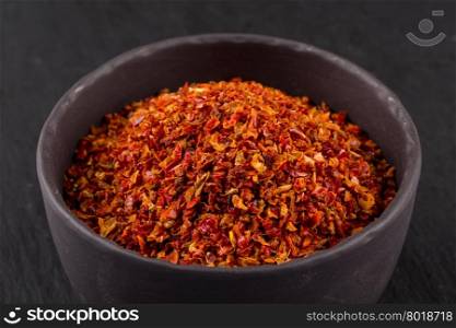 Crushed red chili pepper in stone bowl on dark background