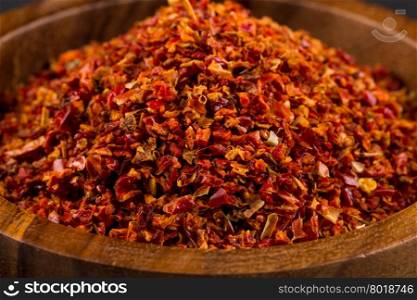 Crushed red chili pepper in wooden bowl on white background