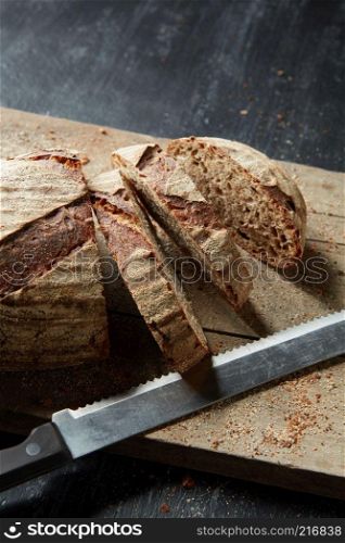 Crusty bread being sliced on an old wooden chopping board on a dark background. Fresh bread on wooden board