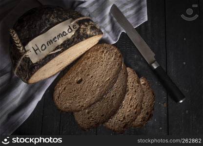Crusty home-baked bread on a black rustic table. Above view with black loaf sliced on a kitchen towel