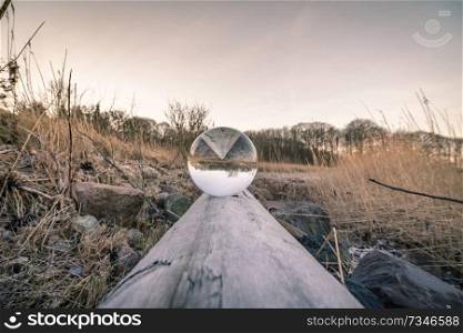 Crystal ball in balance on a wooden log in the nature by a lake